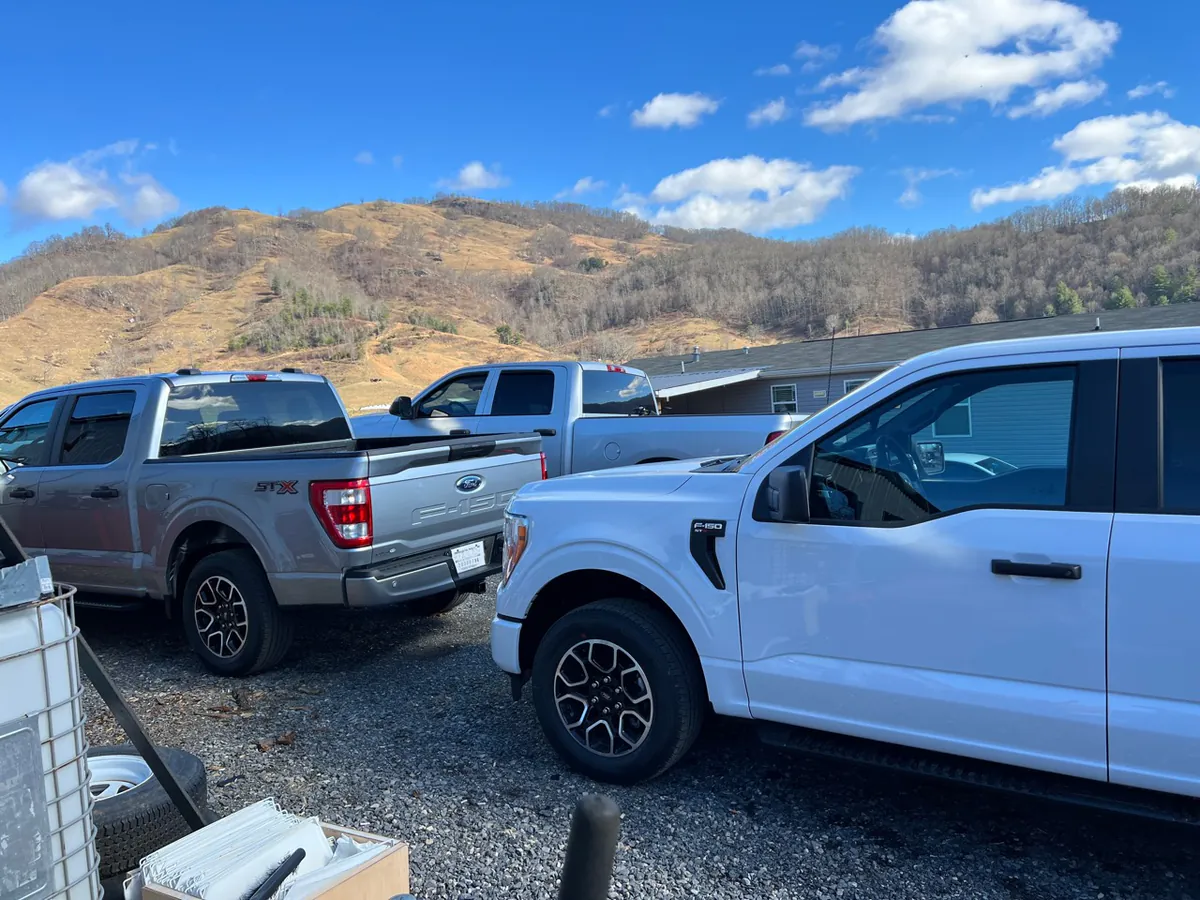 Pickup trucks in the gravel yard at McElroy Auto Repair with Western North Carolina mountains behind them